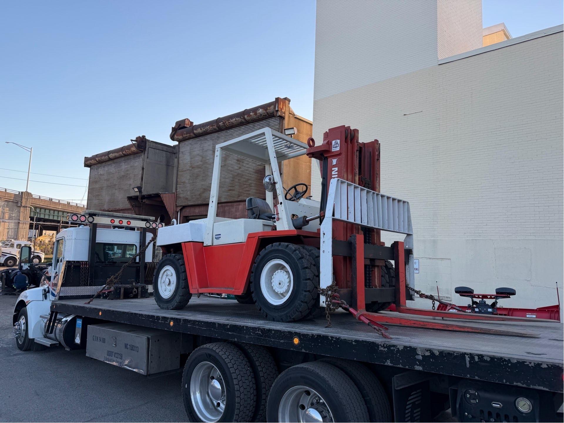 Red and white 15K forklift secured on a flatbed deck, shown in side profile